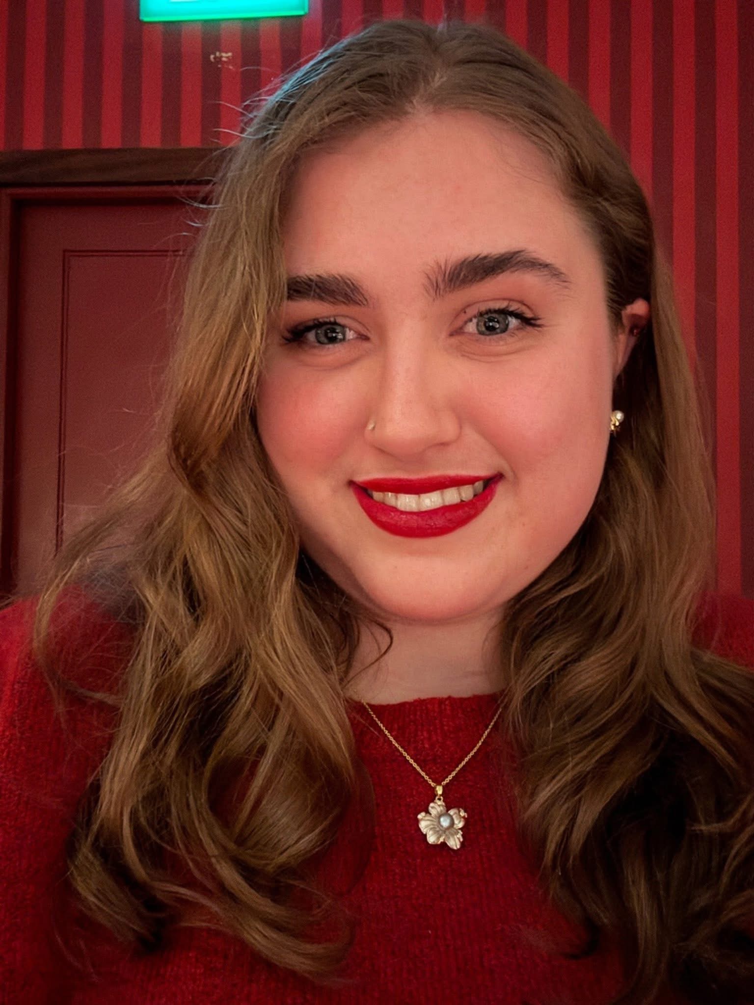 Person wearing red shirt with a gold flower necklace.